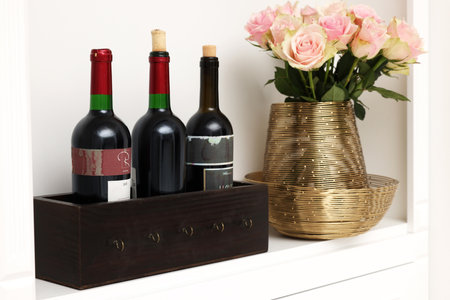 Shelf with different wine bottles and beautiful rose flowers indoorsの写真素材