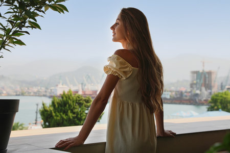 Beautiful young woman with long hair standing on balconyの写真素材