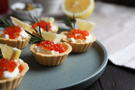 Delicious tartlets with red caviar and cream cheese served on wooden table, closeup. Space for textの写真素材