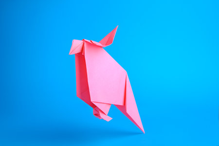 origami art. Handmade pink paper parrot on light blue backgroundの写真素材