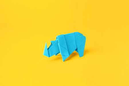 origami art. Handmade light blue paper rhinoceros on yellow backgroundの写真素材