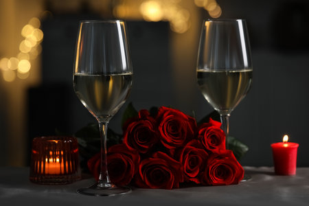 Romantic table setting with glasses of white wine, burning candles and rose flowers against blurred lightsの写真素材
