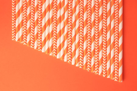 Many striped paper drinking straws on orange background, flat layの写真素材