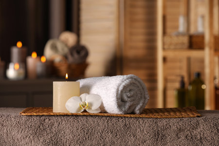 Spa composition with candle, orchid flower and rolled towel on massage table in wellness center, space for textの写真素材
