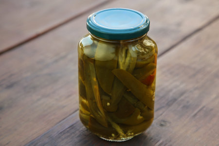 Glass jar of pickled green jalapeno peppers on wooden table, closeupの写真素材