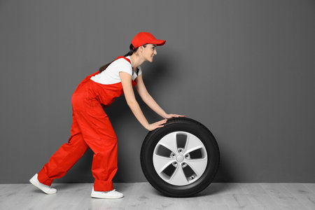 Female mechanic in uniform with car tire on gray wall backgroundの写真素材