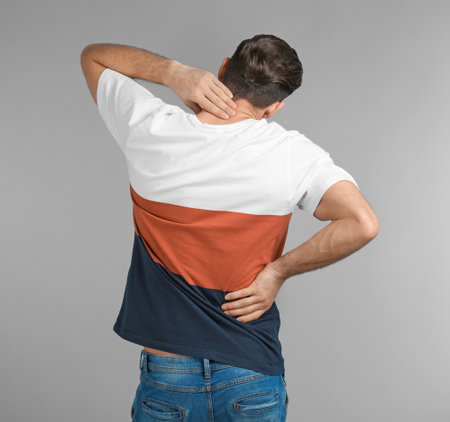 Young man suffering from back pain on gray backgroundの写真素材