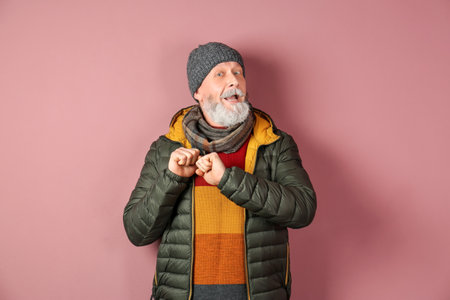 Mature man in warm clothes on color background. Ready for winter vacationの写真素材