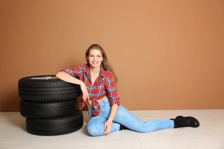 Young woman in seductive outfit with car tires on color wall backgroundの写真素材