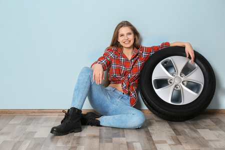Young woman in seductive outfit with car tire on gray wall backgroundの写真素材