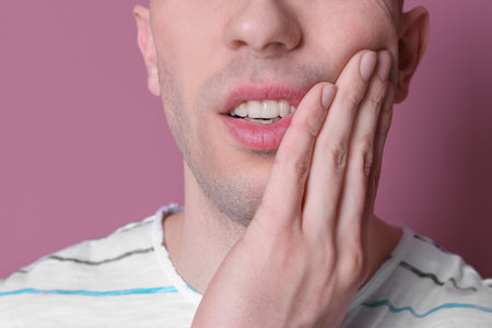 Young man with sensitive teeth on color background, closeupの写真素材