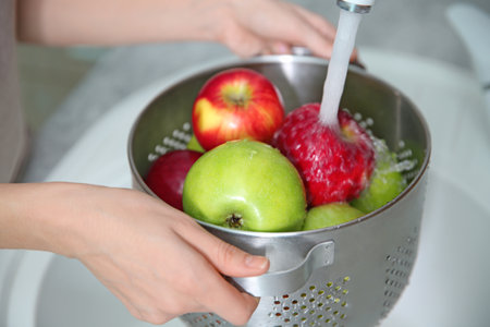 Young woman washing ripe apples in the kitchen