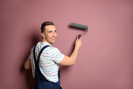 Young male decorator with paint roller near color wallの写真素材