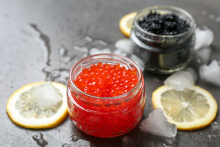 Glass jars with black and red caviar on gray background