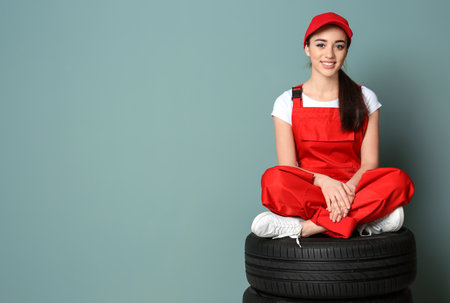 Female mechanic in uniform with car tires on color wall backgroundの写真素材