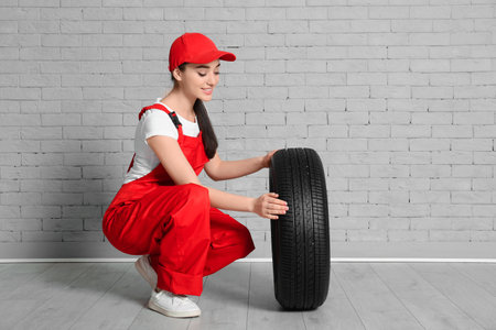 Female mechanic in uniform with car tire against brick wall backgroundの写真素材