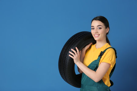 Female mechanic in uniform with car tire on color backgroundの写真素材