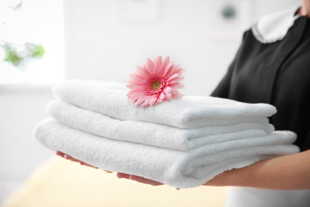 Young maid holding stack of towels and flower in hotel roomの写真素材