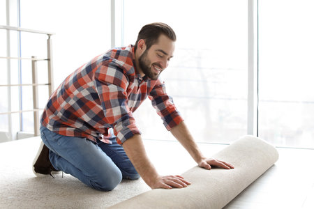 Man rolling out new carpet flooring in roomの写真素材
