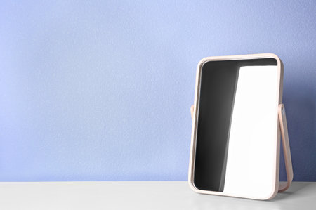Stylish mirror on table near light wallの写真素材