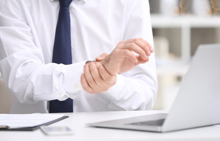 Young man suffering from wrist pain in officeの写真素材