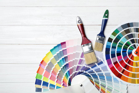 Brushes and color palette samples on wooden background, flat lay