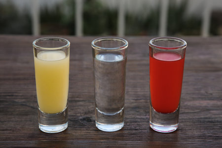 Shots with lime juice, tequila and sangria as colors of mexican flag on wooden table. traditional...