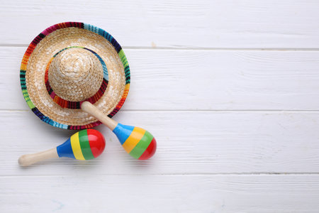 Colorful maracas and sombrero hat on white wooden table, flat lay with space for text. musical...
