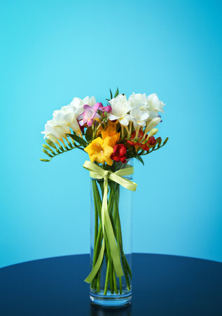 Glass vase with beautiful freesia on table against color backgroundの写真素材