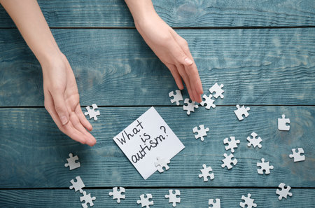 Woman, puzzle pieces and sticky note with phrase "What is autism?" on wooden backgroundの写真素材