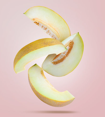 Delicious ripe melon slices falling on light pink backgroundの写真素材