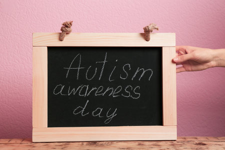 Woman holding blackboard with phrase "Autism awareness day" on color backgroundの写真素材