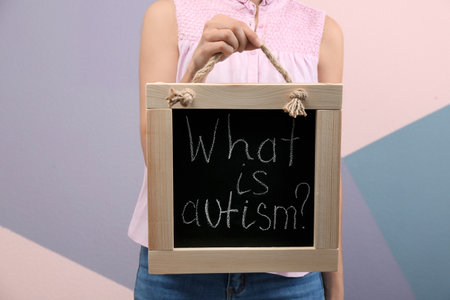 Woman holding blackboard with phrase "What is autism?" color backgroundの写真素材