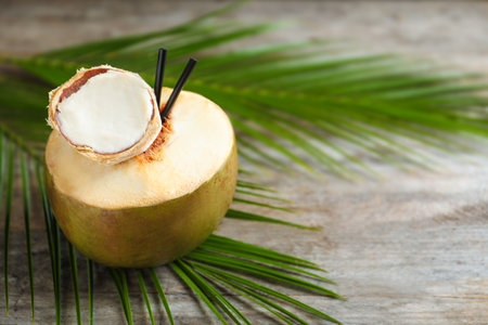Fresh green coconut with drinking straws on wooden table