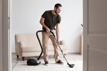 Young man cleaning carpet with vacuum in living roomの写真素材