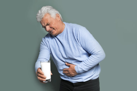 Mature man with dairy allergy holding glass of milk on color backgroundの写真素材