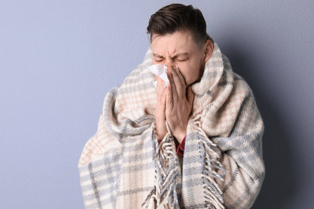 Man wrapped in blanket suffering from cold on color backgroundの写真素材