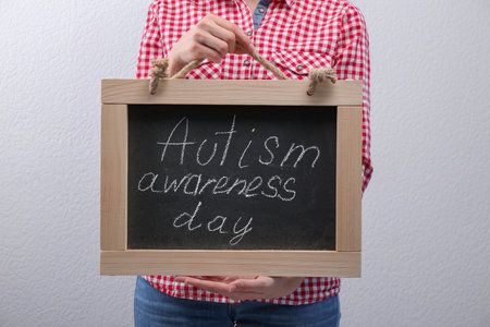 Woman holding blackboard with phrase "Autism awareness day" on light backgroundの写真素材