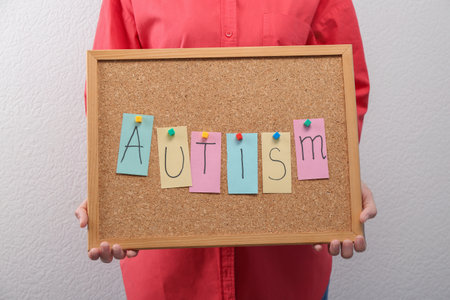 Woman holding board with word Autism on light background