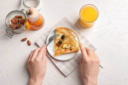 Woman eating thin pancakes with berries and nuts at table, top viewの写真素材