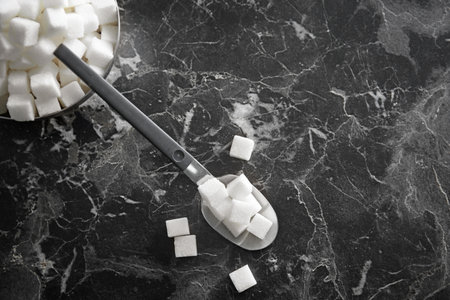 Bowl and spoon with refined sugar cubes on dark gray backgroundの写真素材