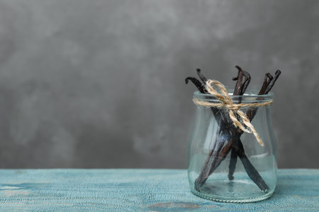 Jar with vanilla sticks on wooden table against gray backgroundの写真素材