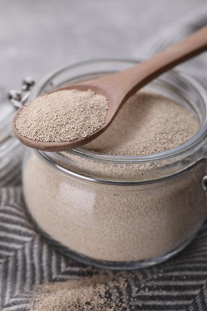 Glass jar and spoon with active dry yeast on light gray table, closeupの写真素材