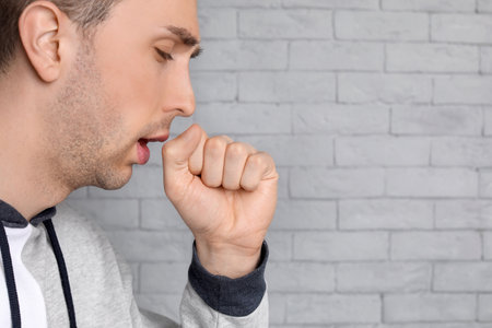 Young man coughing on brick wall backgroundの写真素材