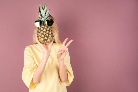 Woman holding pineapple with sunglasses on color backgroundの写真素材