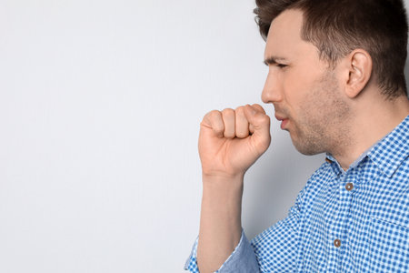 Young man coughing on light backgroundの写真素材