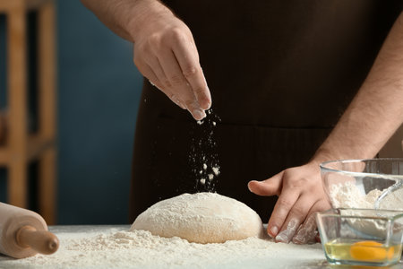 Man sprinkling flour over dough on table in kitchen
