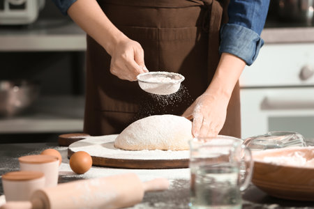Woman sprinkling flour over dough on table in kitchen