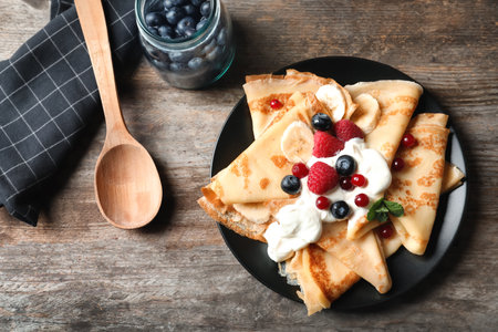 Thin pancakes with berries and cream on plate, top viewの写真素材