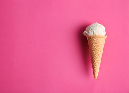 Waffle cone with tasty vanilla ice cream on color background